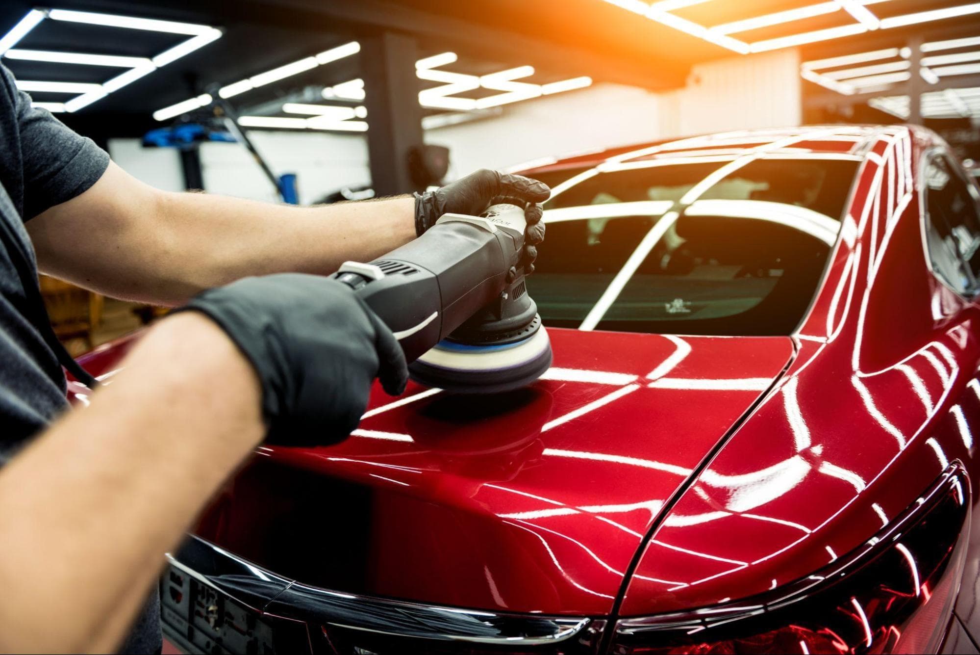 Profissional com luvas realizando polimento no capô de um carro vermelho